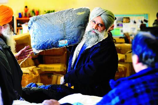 "Organizer Mike Sandhu hands out men's coats at the clothing giveaway Saturday in Tracy at the Larch Clover Community Center." (MICHAELMcCOLLUM/The Record)
