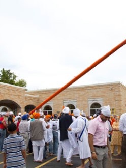 People gather outside the Sikh Temple of Wisconsin for the raising of the Nishan Sahib flag a week after the mass murder that occurred there. A group of about 50 men and boys unwrapped the orange cloth covering the pole, washed the pole with water and milk and then re-wrapped it with a fresh cloth. (source: USA Today)