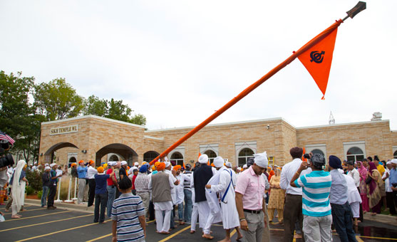 People gather outside the Sikh Temple of Wisconsin for the raising of the Nishan Sahib flag a week after the mass murder that occurred there. A group of about 50 men and boys unwrapped the orange cloth covering the pole, washed the pole with water and milk and then re-wrapped it with a fresh cloth. (source: USA Today)
